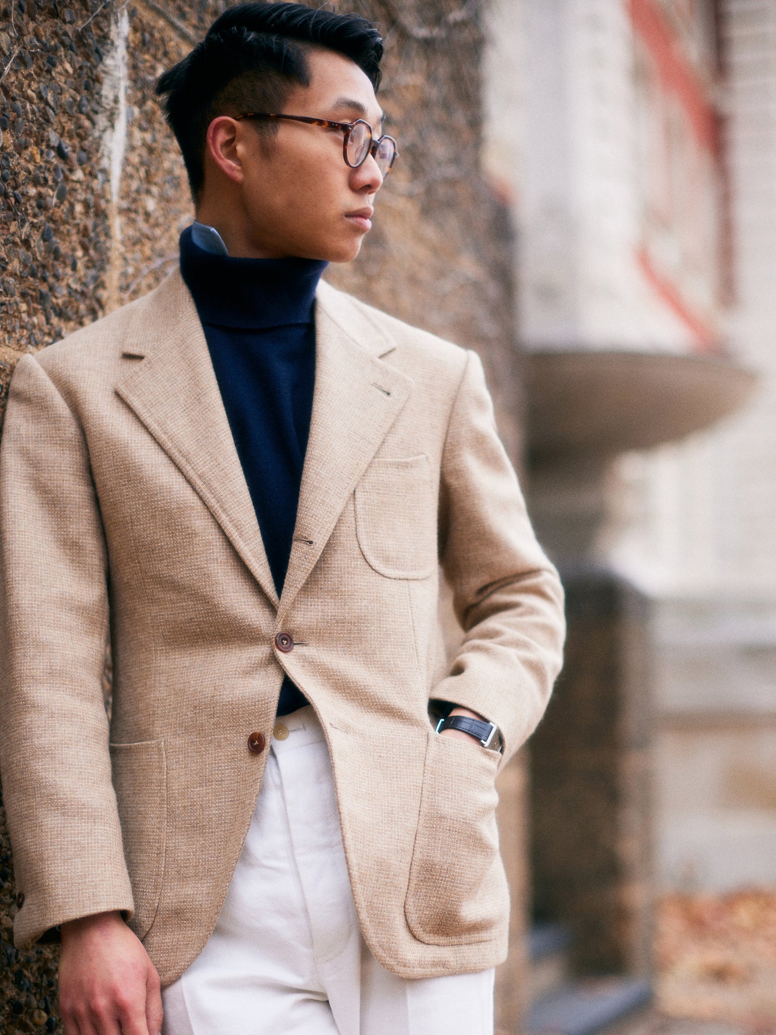 Buzz Tang wearing a light brown overcoat and white trousers with a hand in his pocket, the co-founder of The Anthology, being interviewed by A Collected Man London
