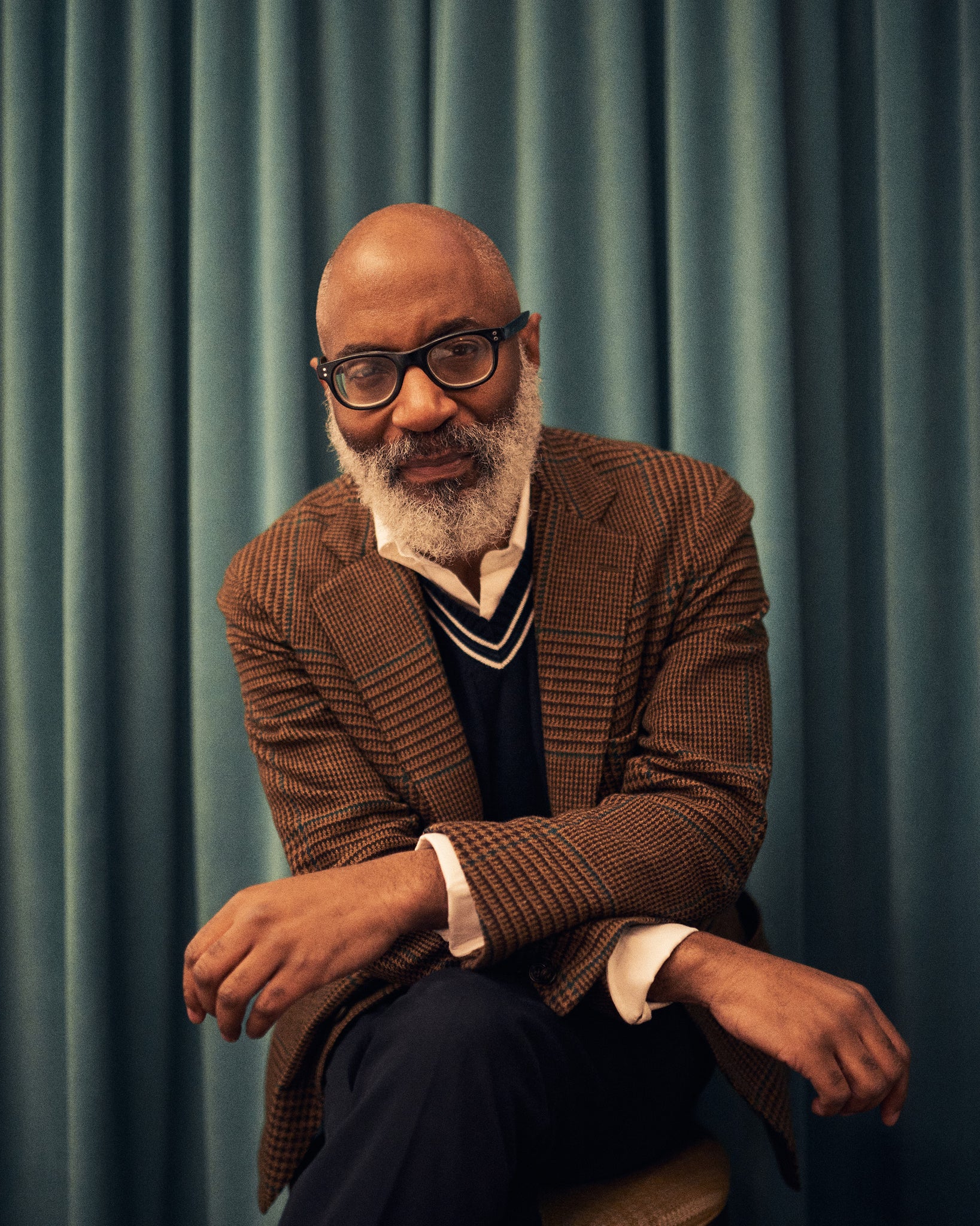 Jason Jules in a brown suit and white collared shirt against the background of a blue curtain, speaking about Ivy Style, African American fashion, jazz, photography, and more. Read the interview now at A Collected Man London.