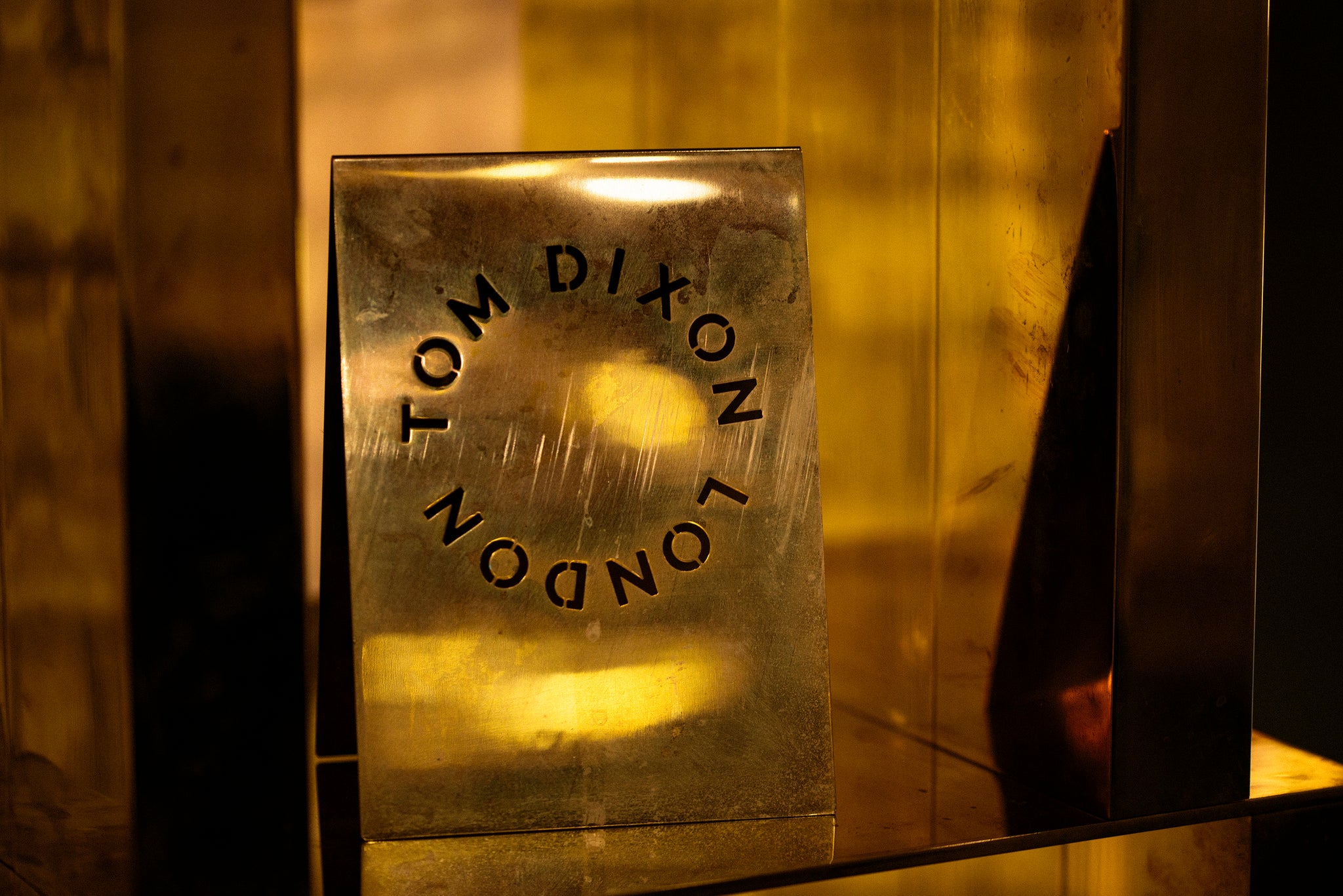 A metal plaque with 'Tom Dixon London' engraved on one side